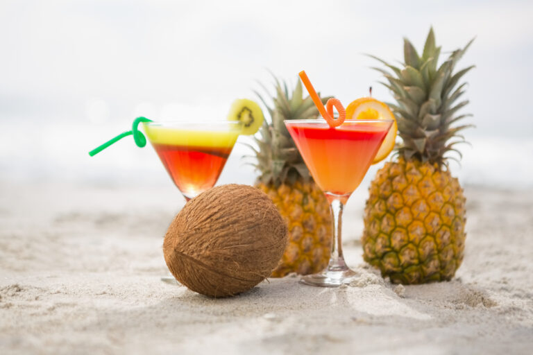 Coconut, pineapples and two glasses of cocktail drink kept on the sand at tropical beach